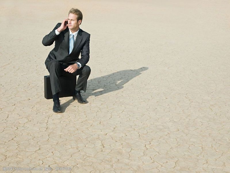 黑色西装干旱地里坐着皮箱打手机的商务男士图片